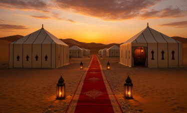 Alt: Campamento de lujo en el desierto de Merzouga con tiendas tradicionales, alfombra roja y faroles iluminados al atardecer en las dunas del Sahara.