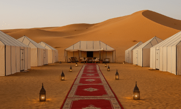 Luxury desert camp in Merzouga with traditional white tents, red carpet, and lanterns surrounded by golden Sahara dunes at sunset.