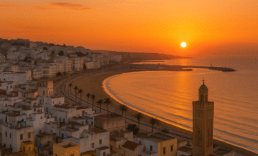 Ciudad de Tánger al atardecer con el sol sobre el océano, la medina y el minarete iluminados en tonos dorados