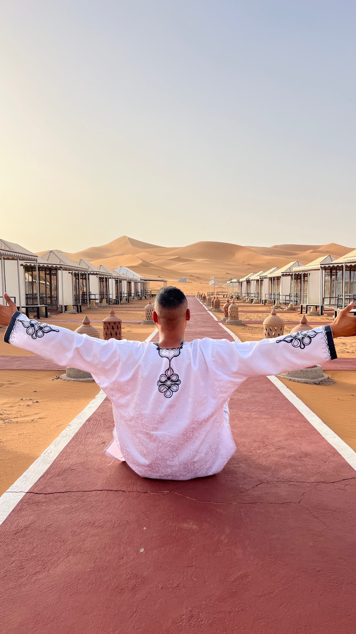 Alt: Campamento de lujo en el desierto de Merzouga con tiendas tradicionales, alfombra roja y faroles iluminados al atardecer en las dunas del Sahara.
